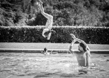 Prince Harry can be seen donning a backwards cap while throwing his daughter in the pool.