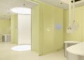 Modern medical room with pale yellow walls, circular lighting, and a sleek design featuring a treatment chair and equipment.