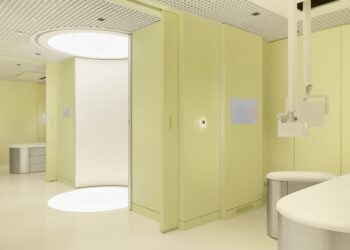 Modern medical room with pale yellow walls, circular lighting, and a sleek design featuring a treatment chair and equipment.