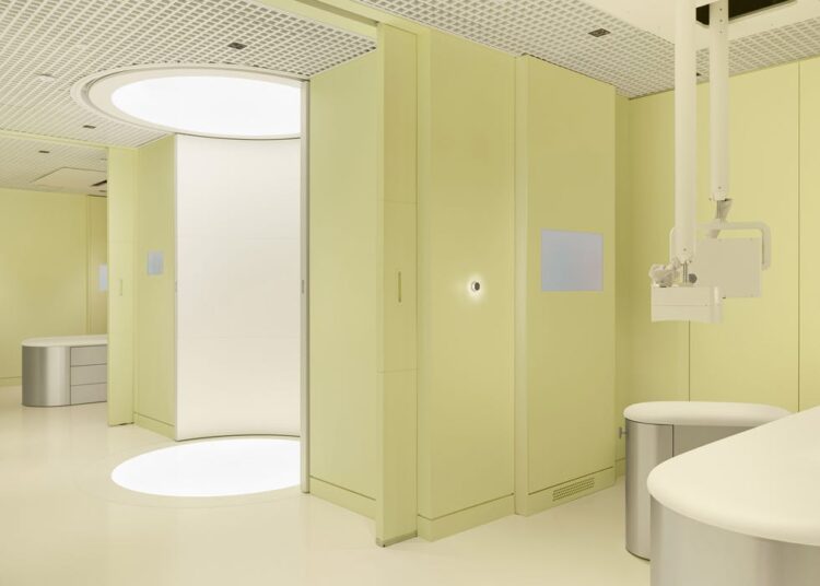 Modern medical room with pale yellow walls, circular lighting, and a sleek design featuring a treatment chair and equipment.