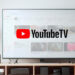 A television displaying the YouTube TV logo sits on a stand in what looks like a living room, the display is surrounded by lights, and multiple devices sit in the cubbies of the stand