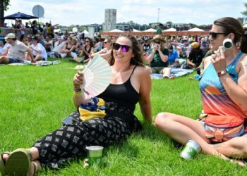 One woman waves a paper fan while another holds an electric fan.