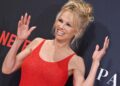 Pamela Anderson puts both her hands up and waves on the red carpet of her Netflix documentary premiere, in a tight red dress