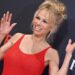 Pamela Anderson puts both her hands up and waves on the red carpet of her Netflix documentary premiere, in a tight red dress