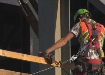 A close-up shot of the back of a construction worker holding a drill while wearing a high-visibility vest.