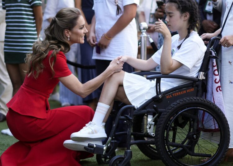 The Princess crouches in front of a girl wearing tennis clothes who is sitting in a wheelchair, and holds her hand