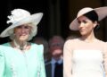 Meghan, Duchess of Sussex, in a white dress and hat, stands next to queen camilla in a green dress and white hat.