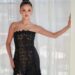 Selena Gomez poses in a strapless black dress with a subtly nude design featuring sheer panels with her hair worn in a high bun