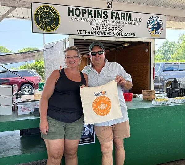 A man and woman pose for a photo at a farm stand at the Electric City Farmers Market in Scranton, PA.