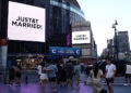 People watch giant screens showing the message "JUST&T MARRIED!" (T&T for Taylor and Travis) outside Madison Square Garden, the reported venue for the wedding celebrations of pop singer Taylor Swift and pro-athlete Travis Kelce, in New York City on July 3, 2026.