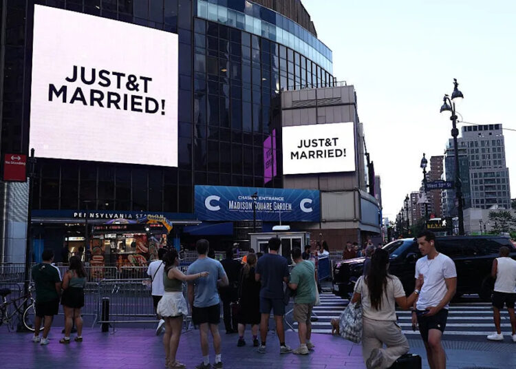 People watch giant screens showing the message "JUST&T MARRIED!" (T&T for Taylor and Travis) outside Madison Square Garden, the reported venue for the wedding celebrations of pop singer Taylor Swift and pro-athlete Travis Kelce, in New York City on July 3, 2026.