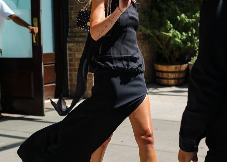 Dakota Johnson styles a halter little black dress with black mule heels and a Valentino spiked bag for Taylor Swift's wedding