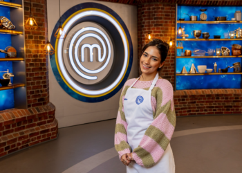 cook wearing apron in a kitchen studio with masterchef logo in background.