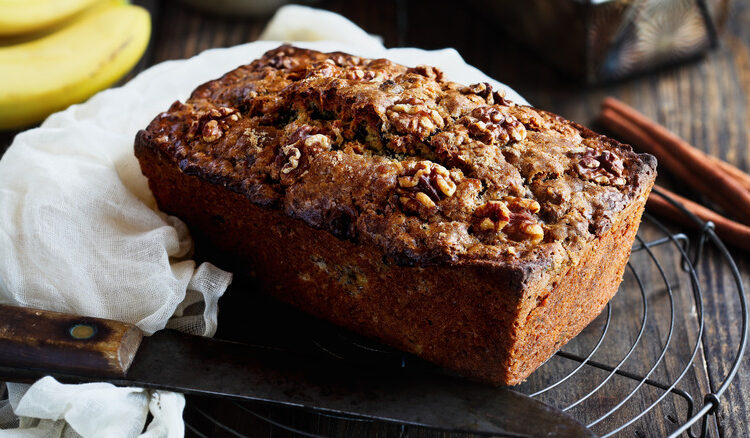 Loaf of walnut banana bread on rack next to knife