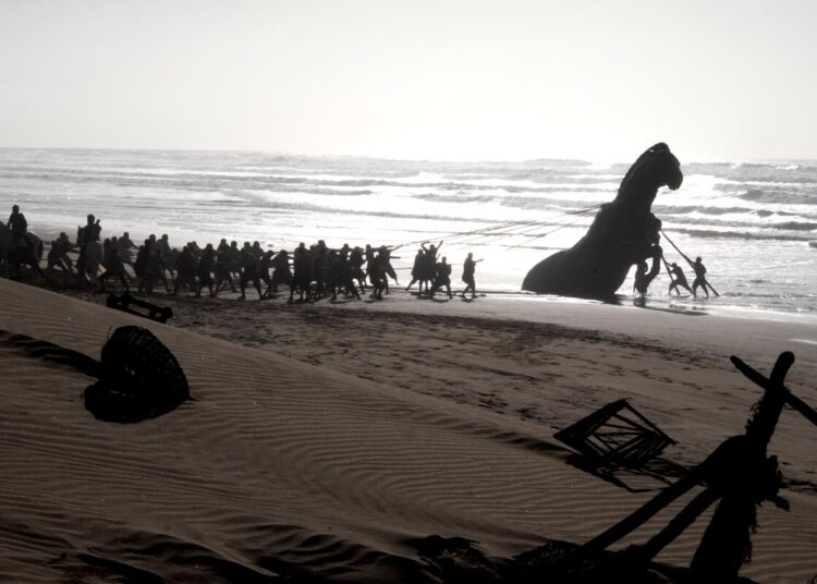 Men pull the Trojan Horse on a beach in "The Odyssey."