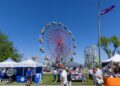 People walk among vendor booths and carnival rides on a sunny day at the San Joaquin County Fairgrounds