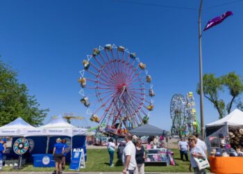 People walk among vendor booths and carnival rides on a sunny day at the San Joaquin County Fairgrounds