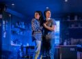 A man and a woman hold on to each other in a low-lit kitchen with fog in the background.