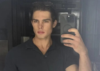 Clavicular taking a mirror selfie with a smartphone, wearing a dark shirt and sunglasses on their head.
