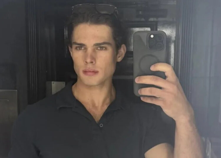 Clavicular taking a mirror selfie with a smartphone, wearing a dark shirt and sunglasses on their head.