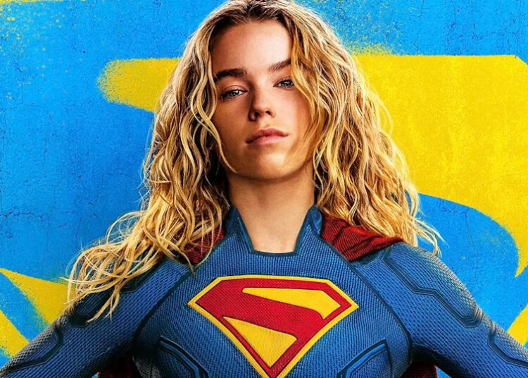 Supergirl in costume in front of blue and yellow logo in Supergirl poster.