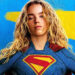 Supergirl in costume in front of blue and yellow logo in Supergirl poster.