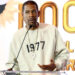 Young Guru in a beige sweatshirt with "1977" printed on it speaks at a podium. The background features floral designs and large text.