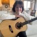 Shawna Edwards - compositora de "Porque," uma nova adição aos Hinos — Para o Lar e a Igreja — posa para uma foto com um violão em Lehi, Utah, janeiro de 2025.