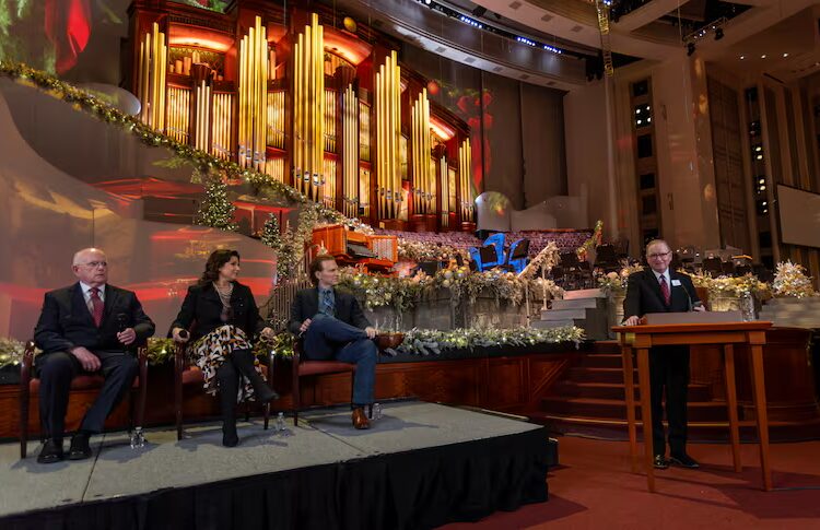 Mack Wilberg, Stephanie J. Block and Sebastian Arcelus sit on a platform as President Gary B. Porter speaks from a podium, during a news conference in the Conference Center in Salt Lake City on Friday, Dec. 12, 2025.