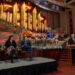 Mack Wilberg, Stephanie J. Block and Sebastian Arcelus sit on a platform as President Gary B. Porter speaks from a podium, during a news conference in the Conference Center in Salt Lake City on Friday, Dec. 12, 2025.