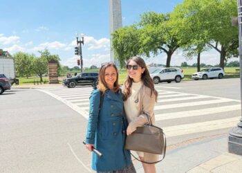 Dos mujeres posando para una foto fuera del Monumento a Washington en un día soleado