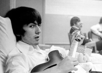 George Harrison tocando la guitarra en un sillón