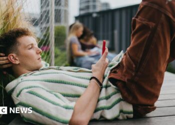 A young man lying down on the ground holding and scrolling on his smartphone.