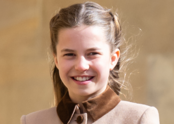 Princess Charlotte wears a light brown coat with a dark collar and smiles