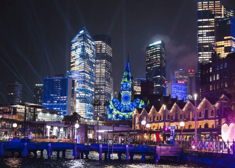 Una proyección de luz brilla sobre la torre del reloj y el horizonte de la ciudad de Sydney.