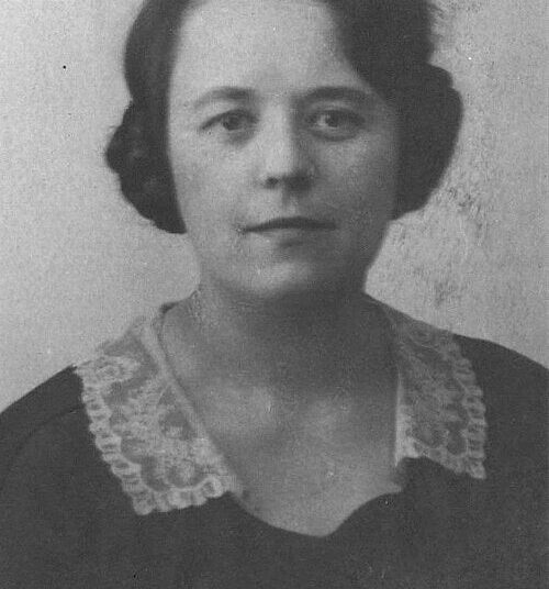 Retrato en blanco y negro de una mujer con cabello corto y oscuro, vestida con un vestido oscuro con un cuello de encaje claro, frente a la cámara sobre un fondo liso.