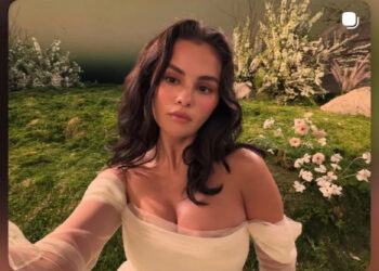 Persona con un vestido blanco posando al aire libre con flores y vegetación.