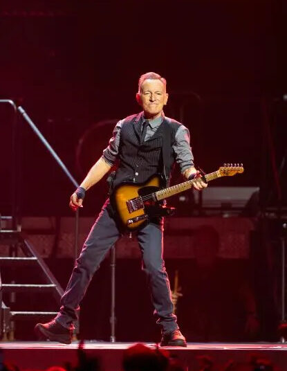 Bruce Springsteen sostiene una guitarra frente a las escaleras mientras está de pie en un escenario.