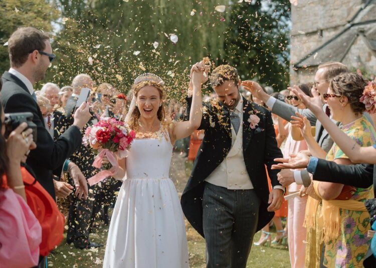 La novia y el novio reciben una lluvia de confeti por parte de familiares y amigos cuando salen de la Iglesia de Todos los Santos, Hovingham.