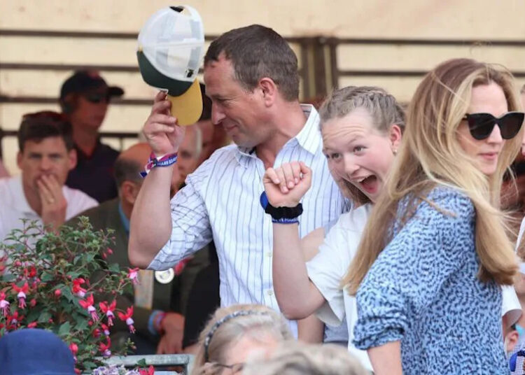 Peter Phillips se quita la gorra mientras Harriet Sperling luce un vestido azul y gafas de sol un poco más abajo.