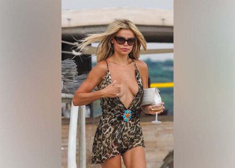 Brooks Nader camina descalza por la playa de Saint-Tropez con un mono corto con estampado de leopardo y sandalias de tacón negras mientras experimenta un mal funcionamiento accidental de su vestuario.