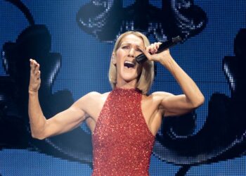Celine Dion cantando frente a un micrófono, con un vestido rojo de lentejuelas, sin mangas y con cuello alto.