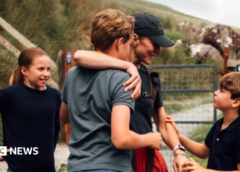 Charlotte looks at her mum who has an arm around George and is being held on the other arm by Louis who she smiles at