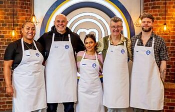 El grupo de cinco concursantes de Masterchef con delantales blancos parados en fila y sonriendo a la cámara.