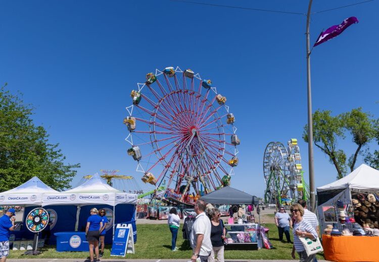 La gente camina entre puestos de vendedores y atracciones de carnaval en un día soleado en el recinto ferial del condado de San Joaquín