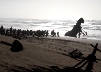 Hombres tiran del caballo de Troya en una playa de "La Odisea."