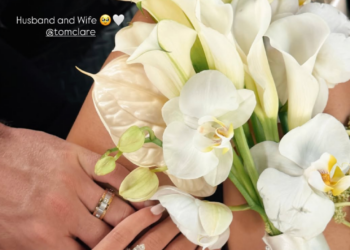 manos con anillos de boda sosteniendo un ramo de flores blancas.