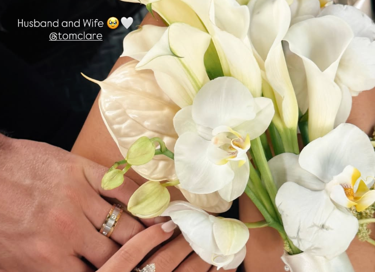 manos con anillos de boda sosteniendo un ramo de flores blancas.